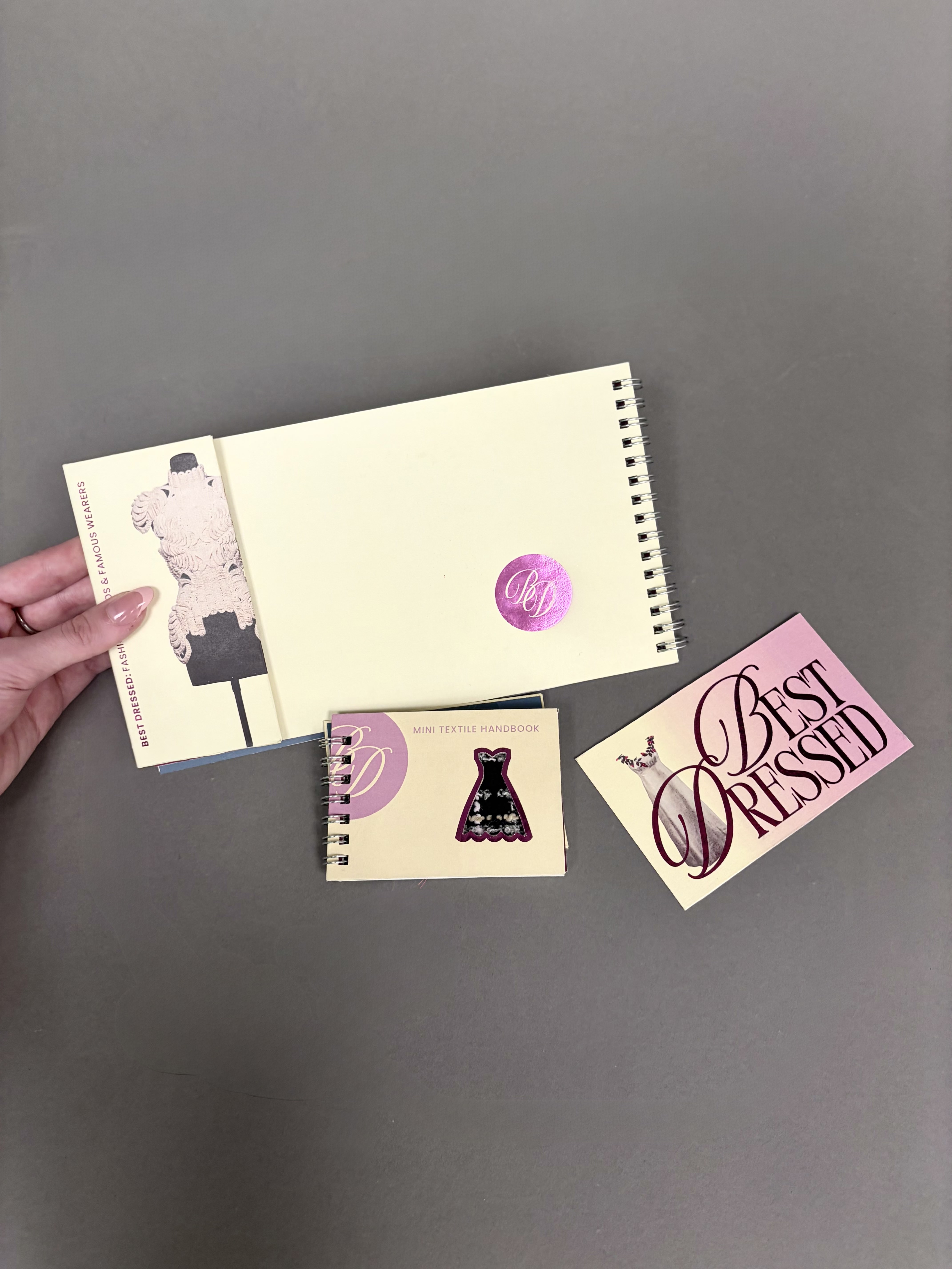 A hand holding the back of the larger book sat next to the donation card and textile handbook.