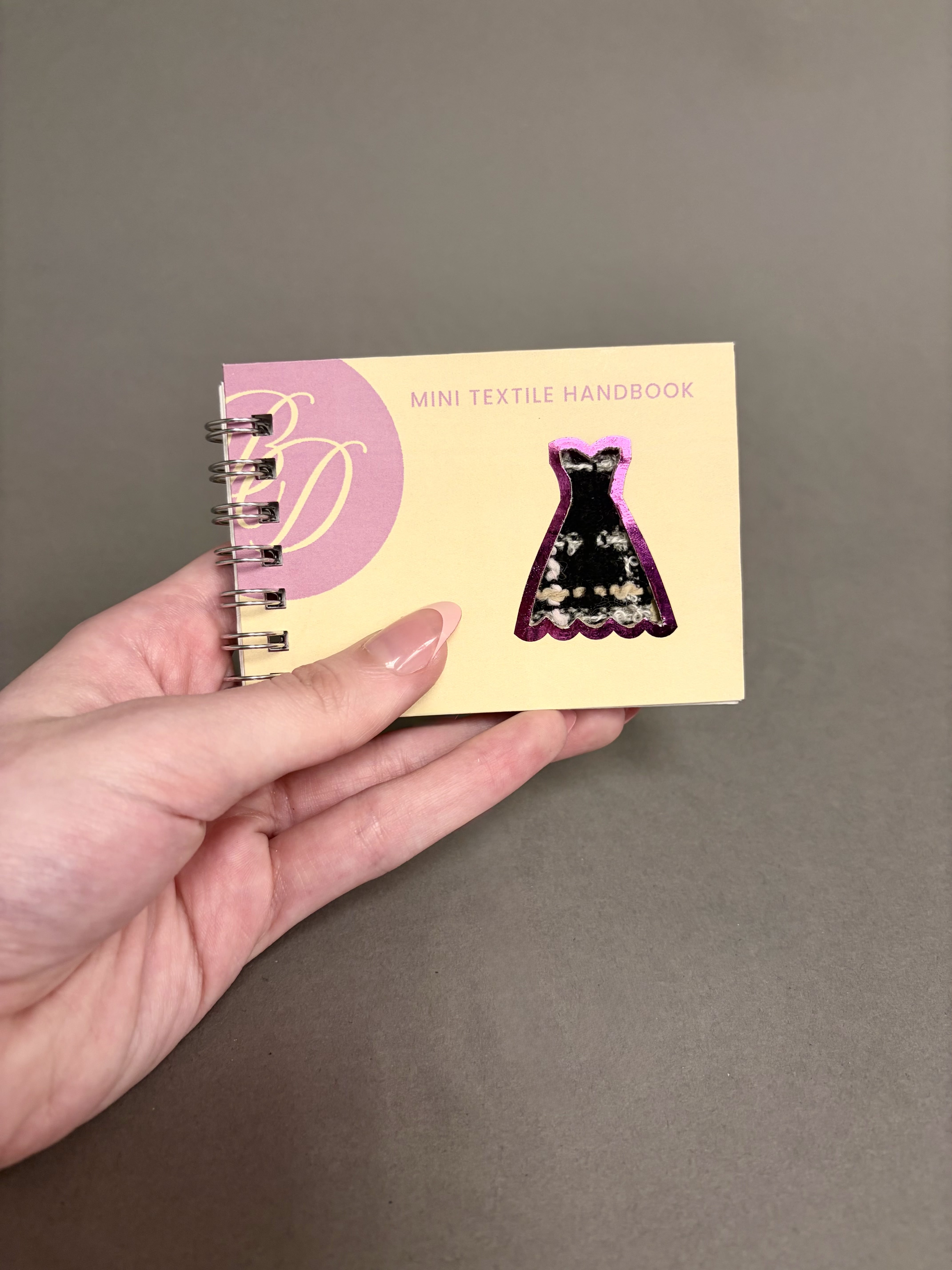 A hand holding the mini textile handbook.
